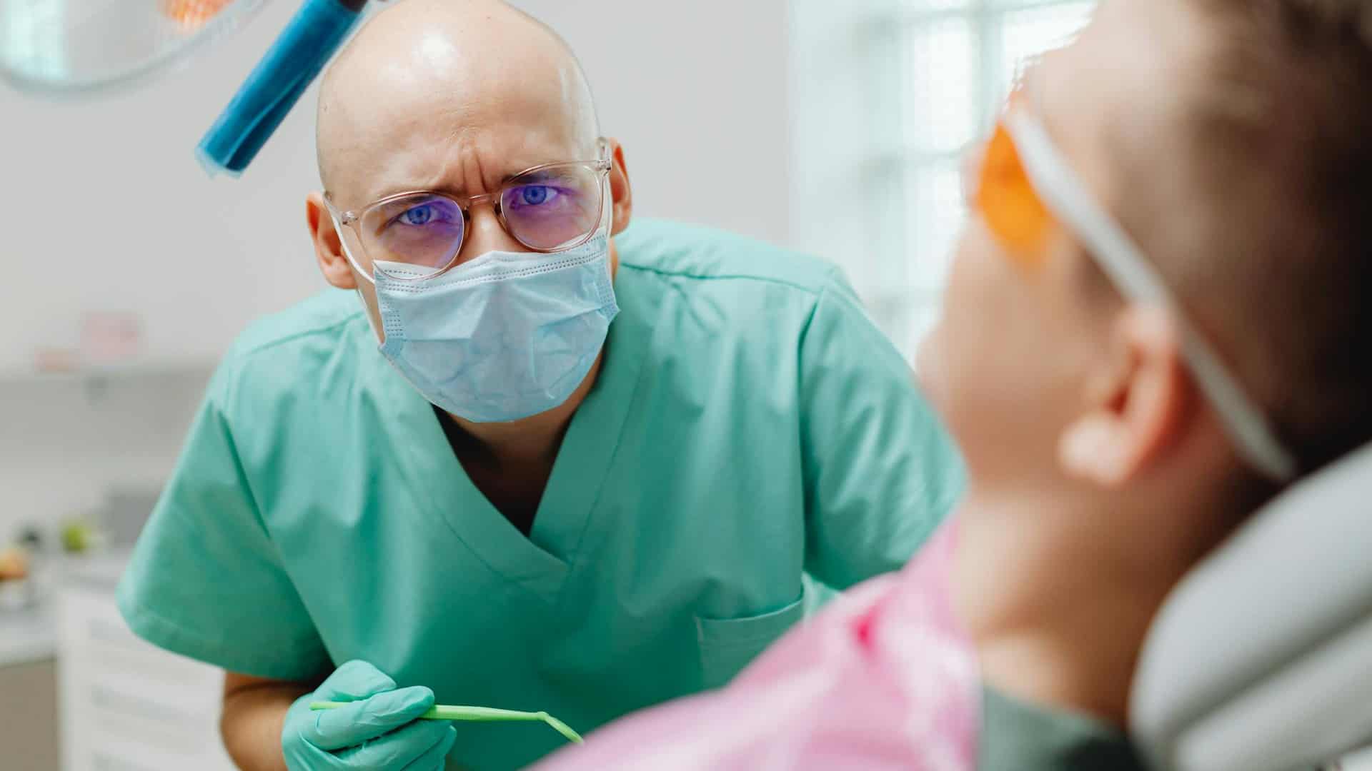 A photograph of a dental care professional looking concernedly in the direction of the viewer while treating a patient, as if disturbed by the question "what happens if you never go to the dentist"