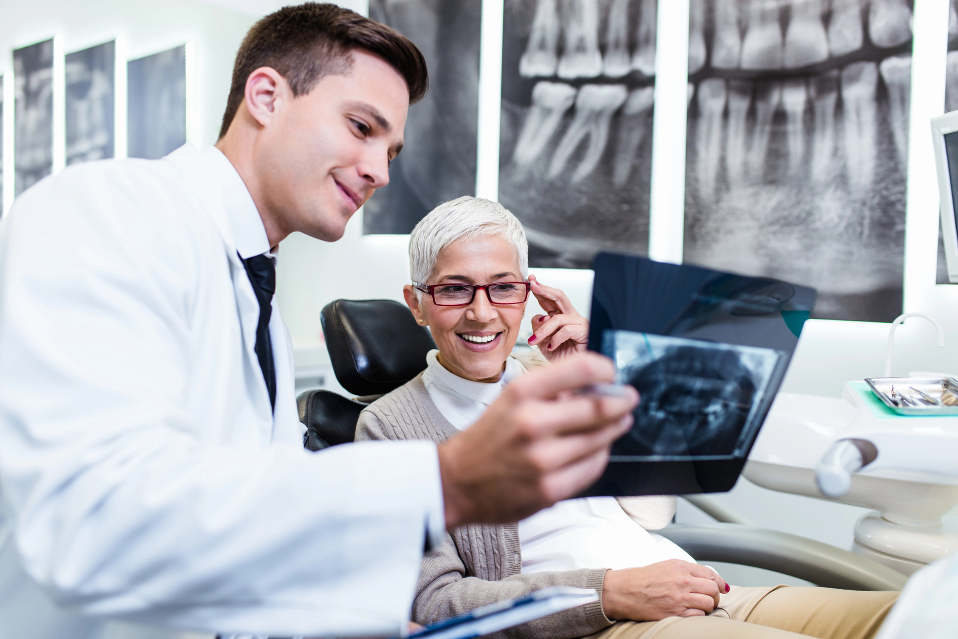 A young male dentist showing an x-ray chart to a senior woman in a dental treatment chair and explaining how it relates to dental implant pre-treatments